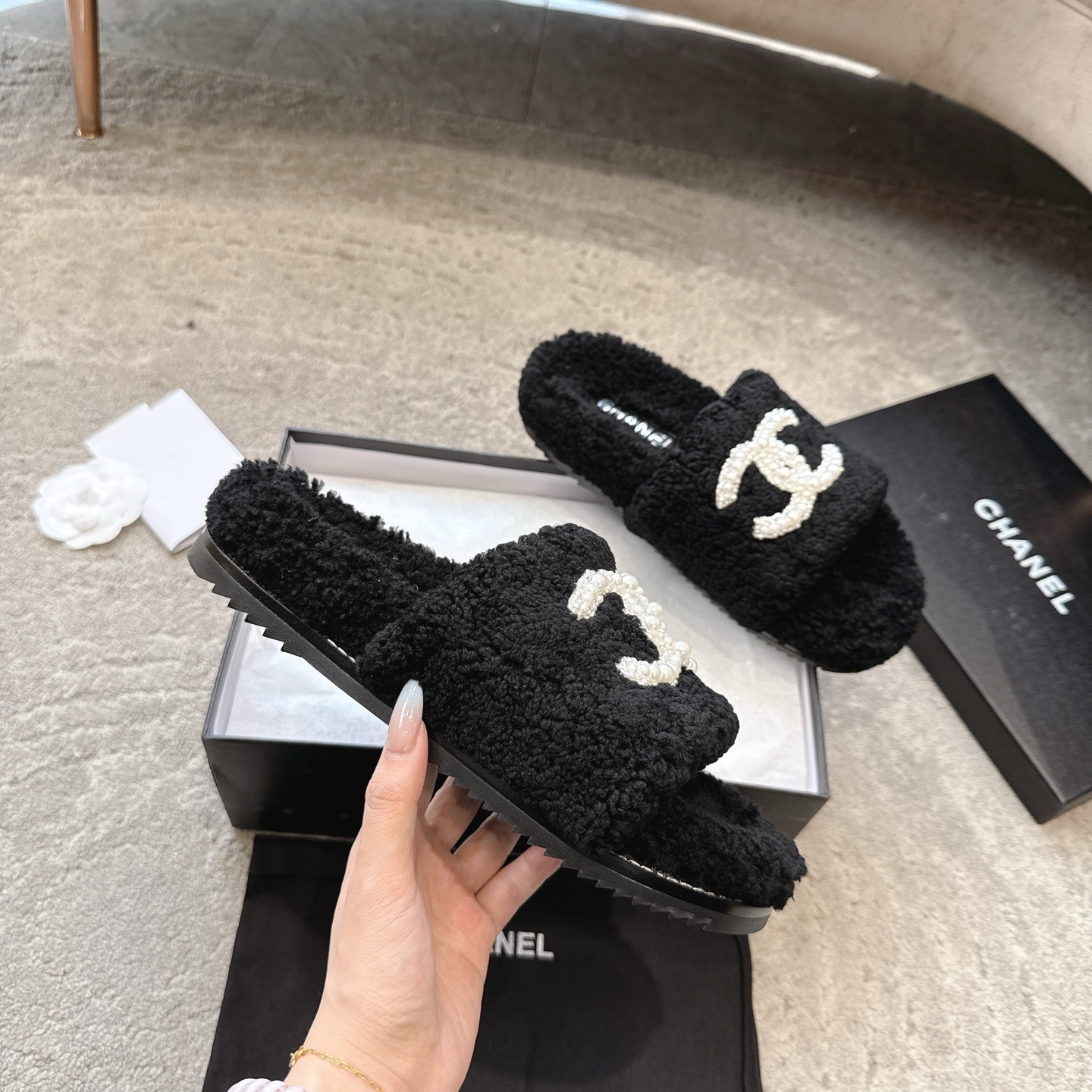 A pair of black fuzzy Chanel shearling slides with a large white pearl-embellished interlocking CC logo on the strap, shown in their original box. - Hình 3