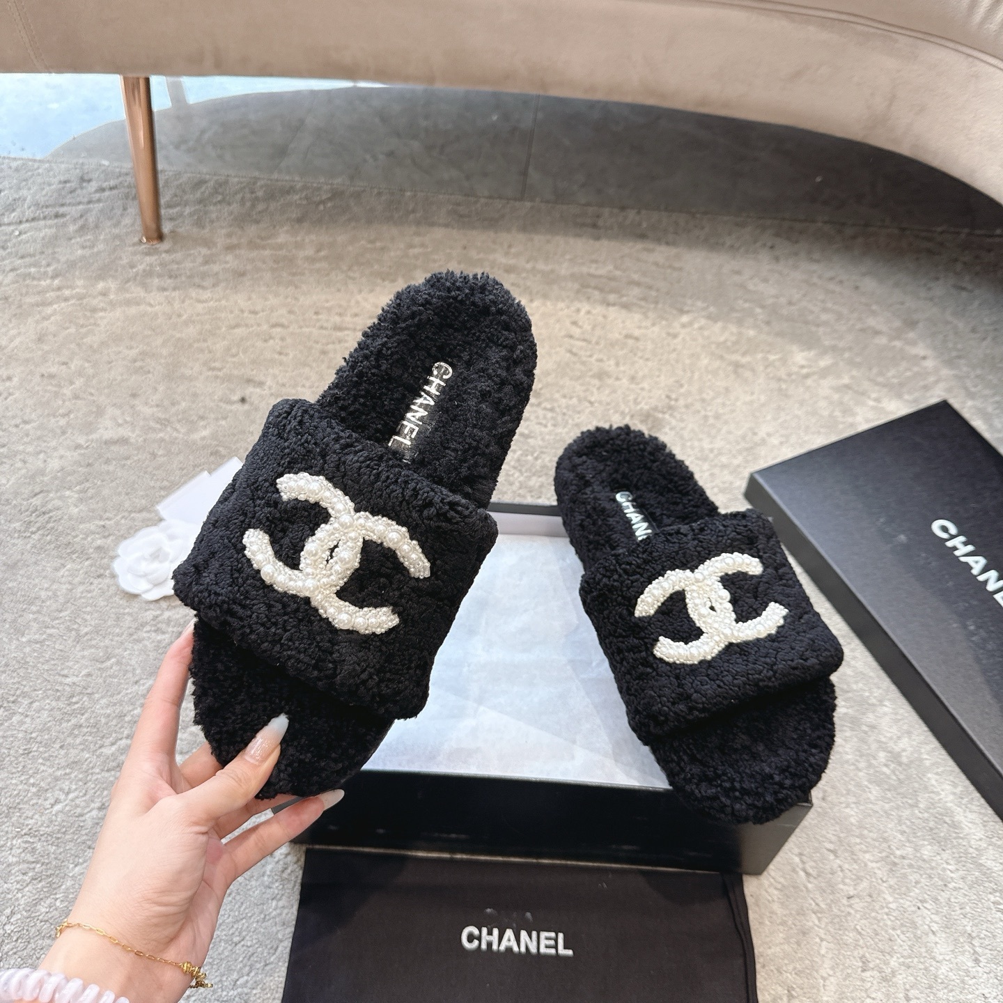 A pair of black fuzzy Chanel shearling slides with a large white pearl-embellished interlocking CC logo on the strap, shown in their original box. - Hình 2
