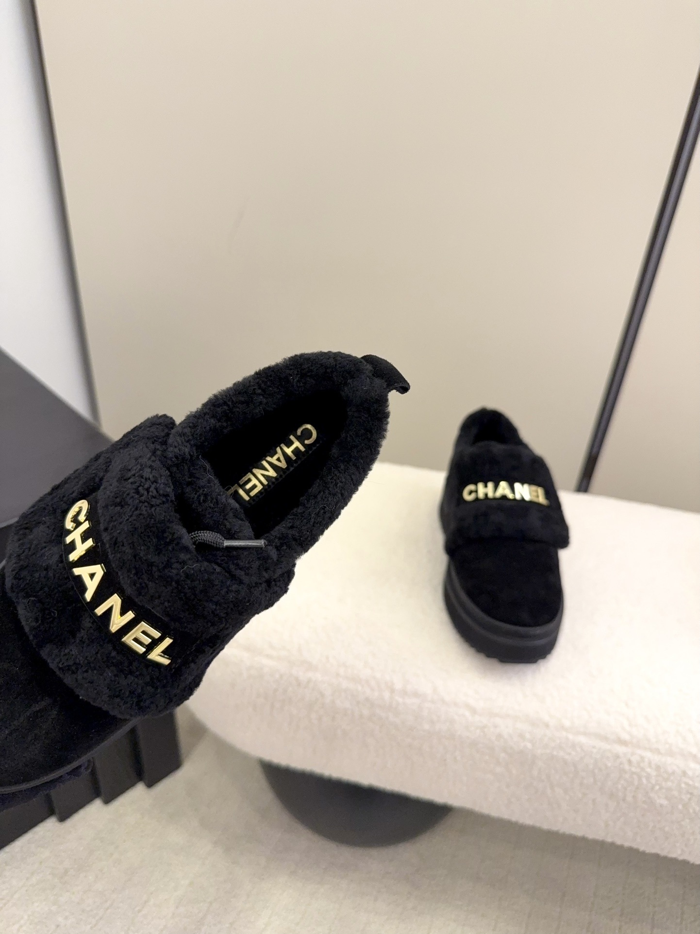 Pair of black Chanel shearling platform loafers with gold logo lettering on a white textured surface - Hình 6