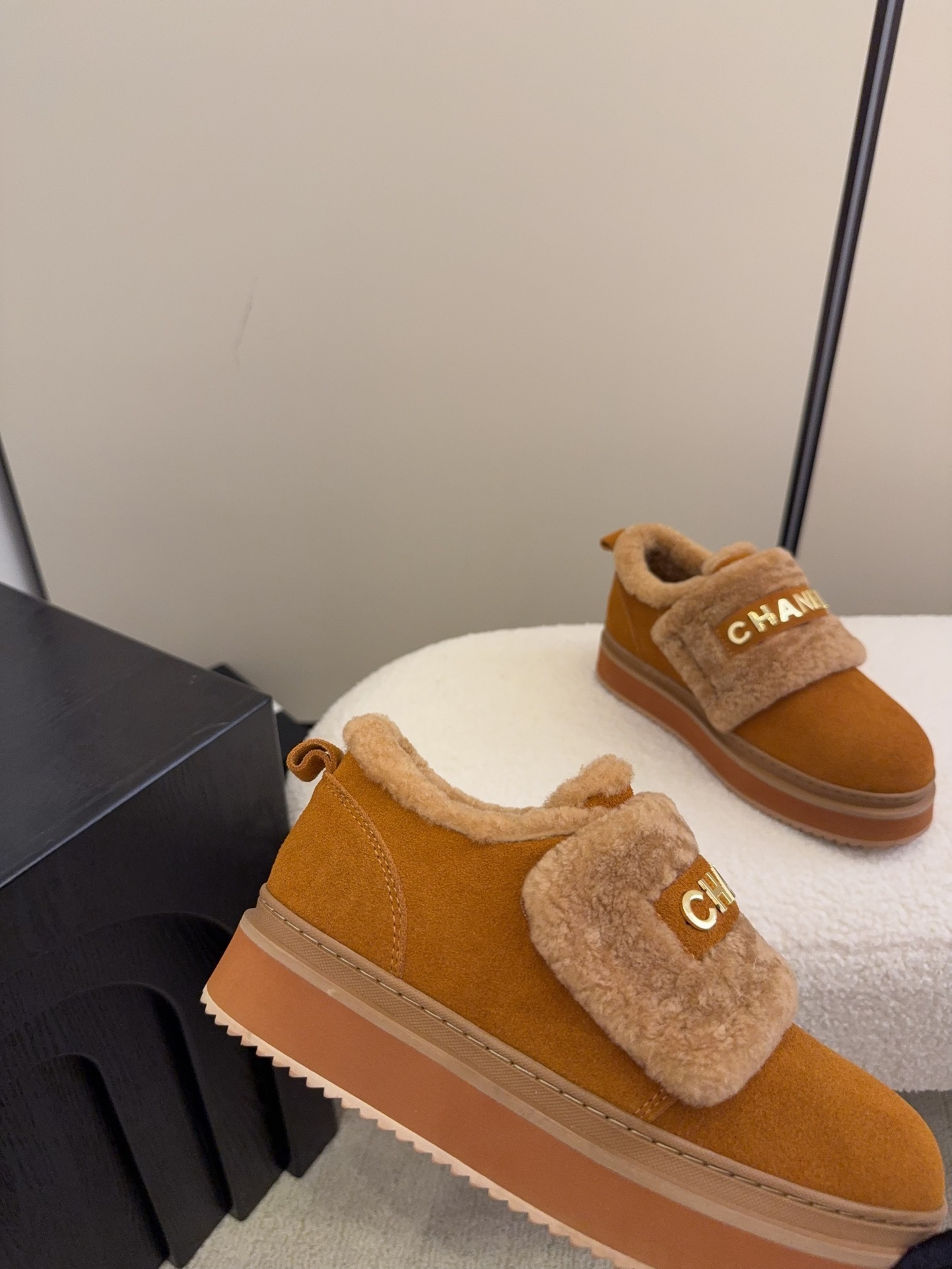 Pair of tan Chanel suede platform sneakers with shearling lining and gold logo strap on a white textured surface. - Hình 4