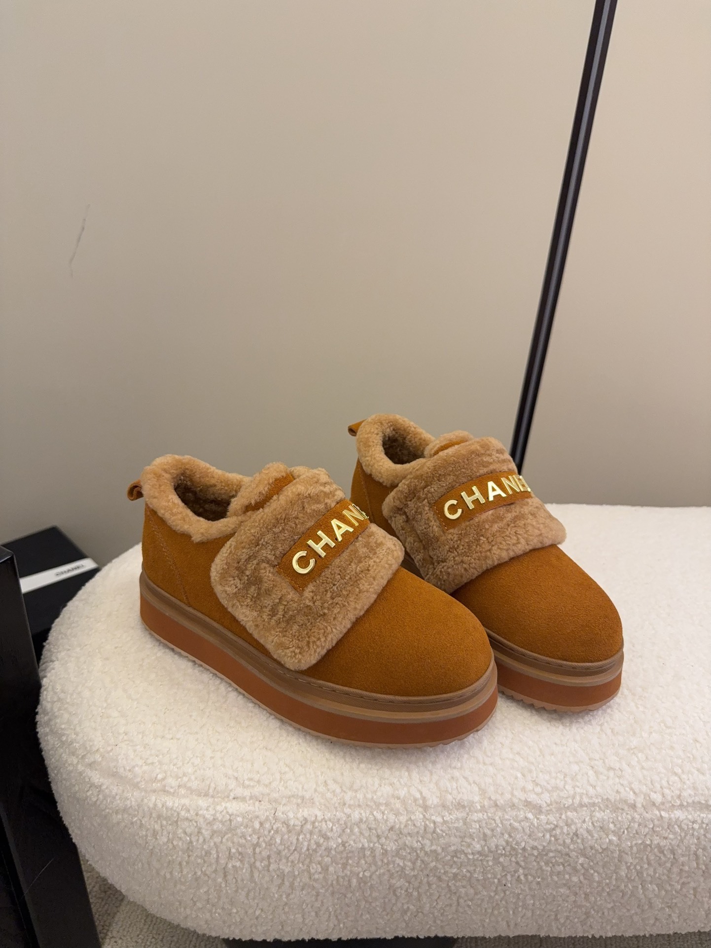 Pair of tan Chanel suede platform sneakers with shearling lining and gold logo strap on a white textured surface. - Hình 2