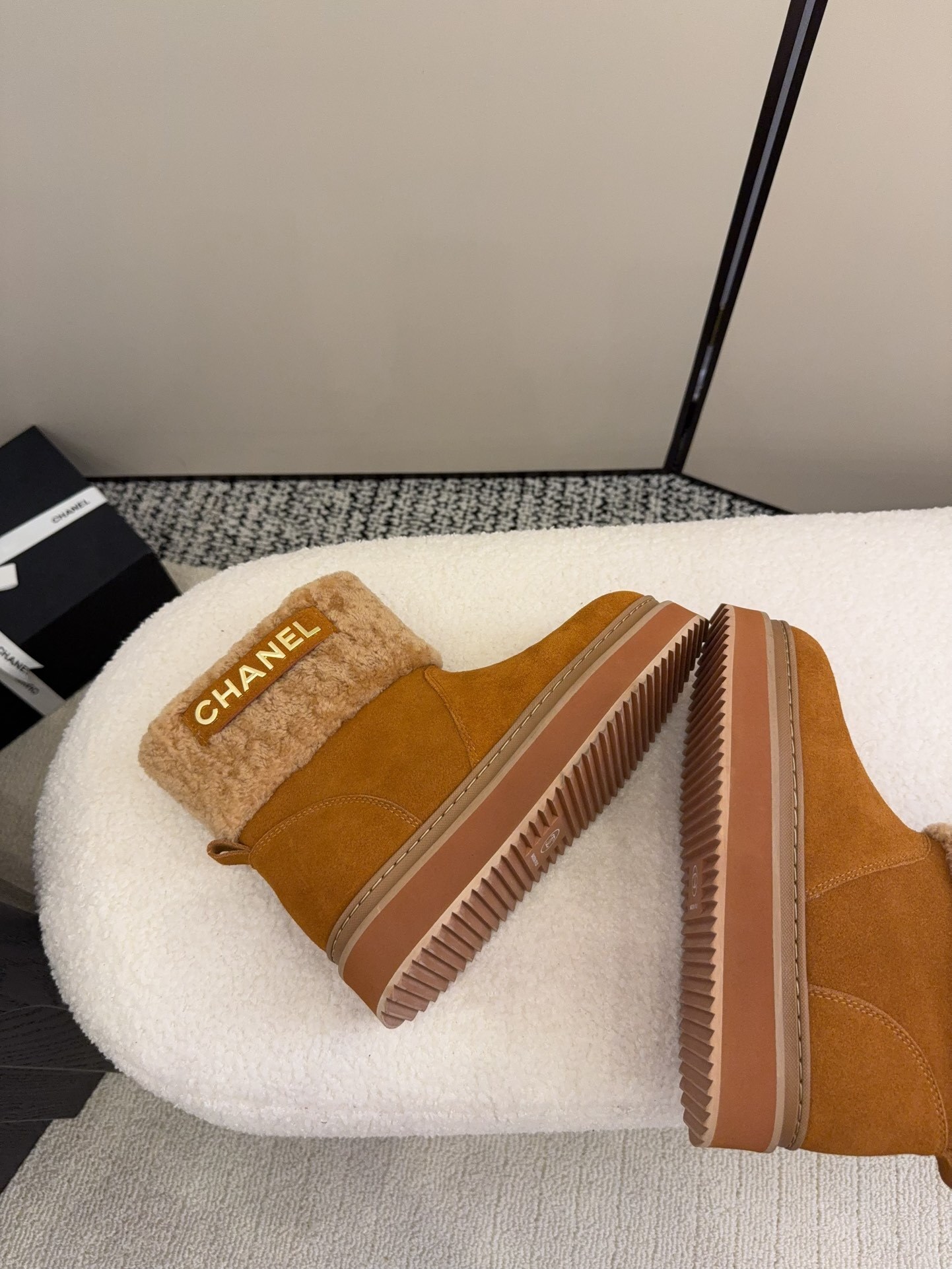 A pair of camel-colored Chanel suede platform boots with tan shearling trim and gold logo detail on a white textured surface. - Hình 9