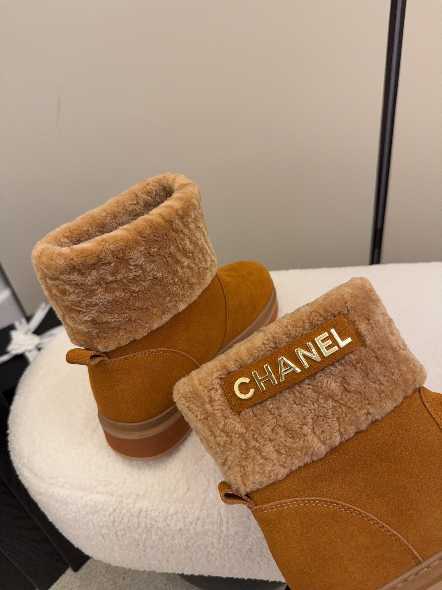 A pair of camel-colored Chanel suede platform boots with tan shearling trim and gold logo detail on a white textured surface. - Hình 8