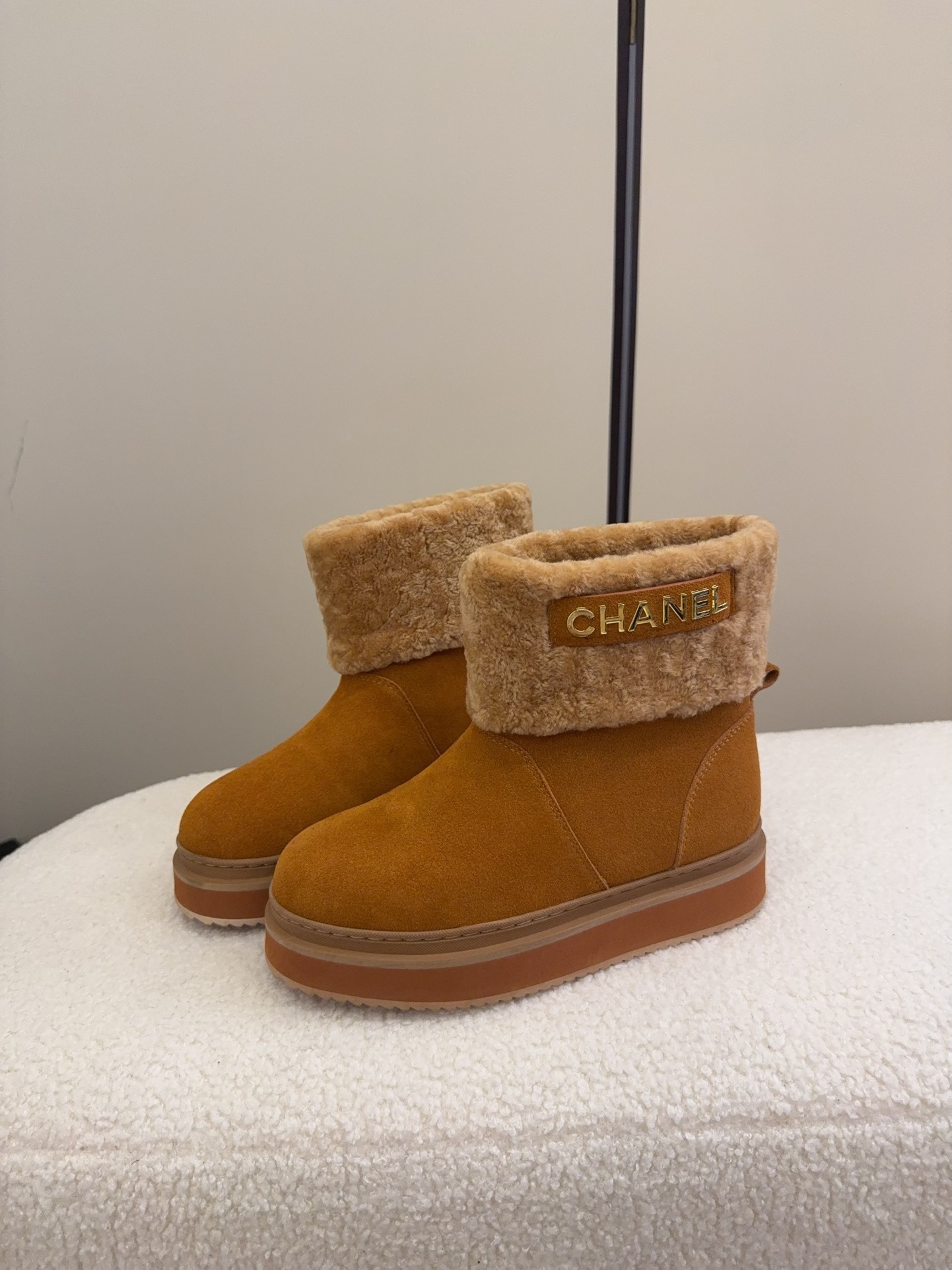 A pair of camel-colored Chanel suede platform boots with tan shearling trim and gold logo detail on a white textured surface. - Hình 7