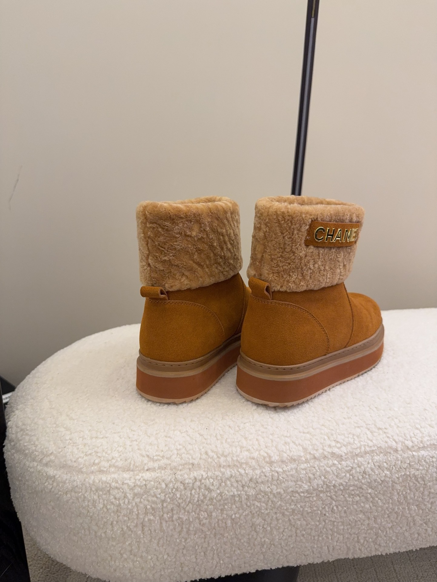 A pair of camel-colored Chanel suede platform boots with tan shearling trim and gold logo detail on a white textured surface. - Hình 5