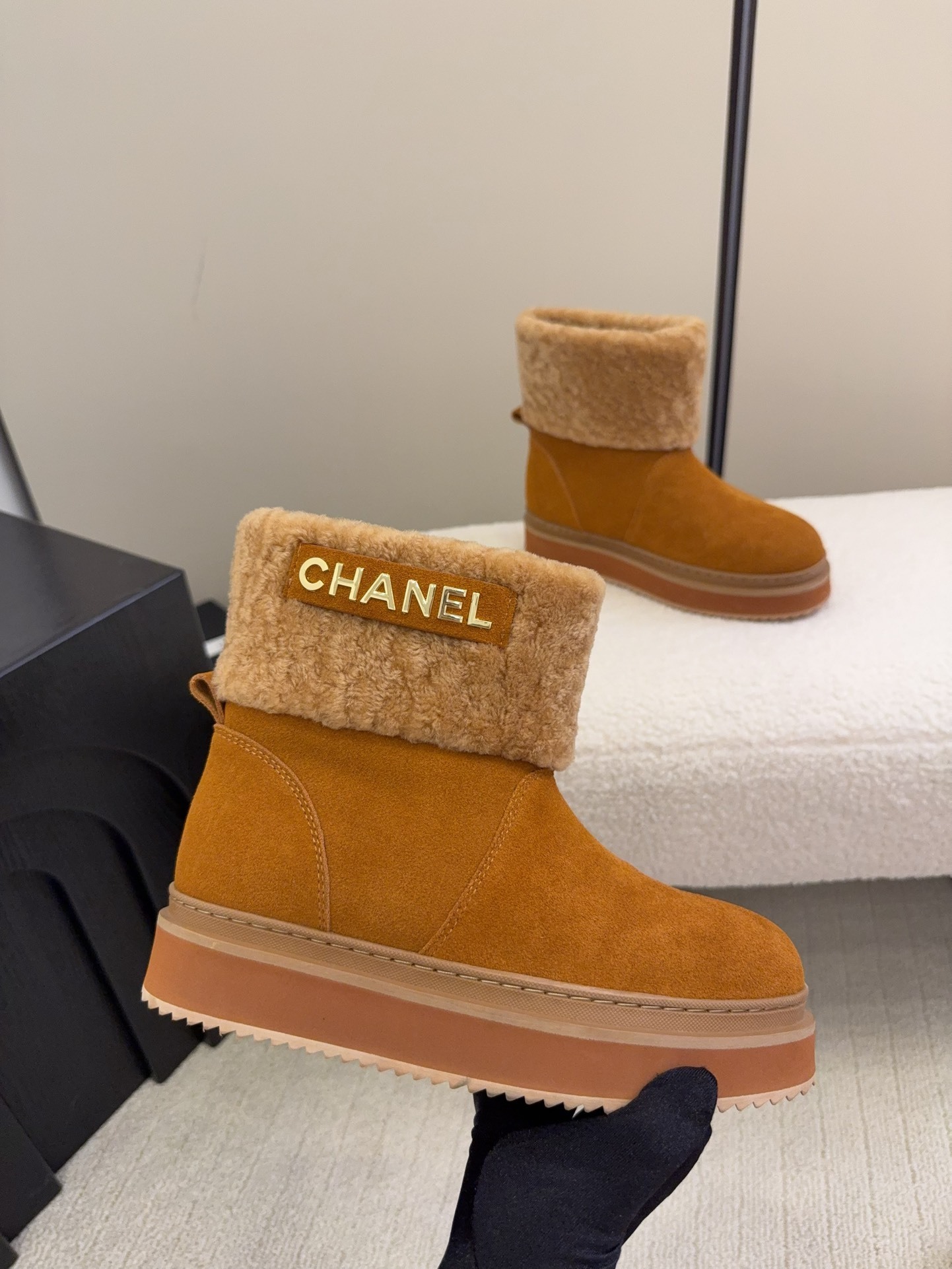 A pair of camel-colored Chanel suede platform boots with tan shearling trim and gold logo detail on a white textured surface. - Hình 4