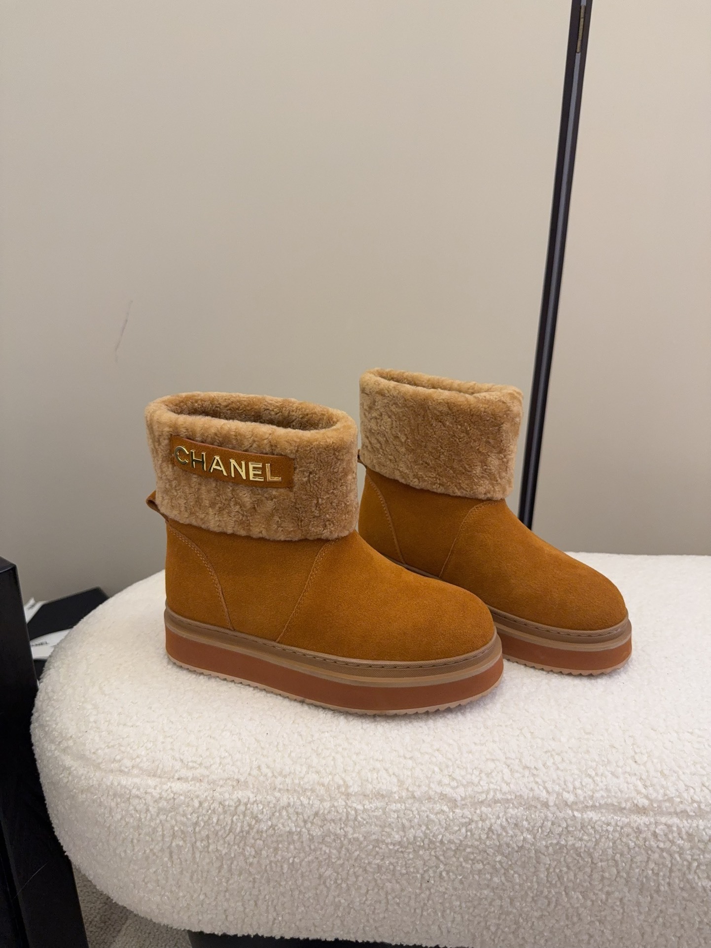 A pair of camel-colored Chanel suede platform boots with tan shearling trim and gold logo detail on a white textured surface. - Hình 2