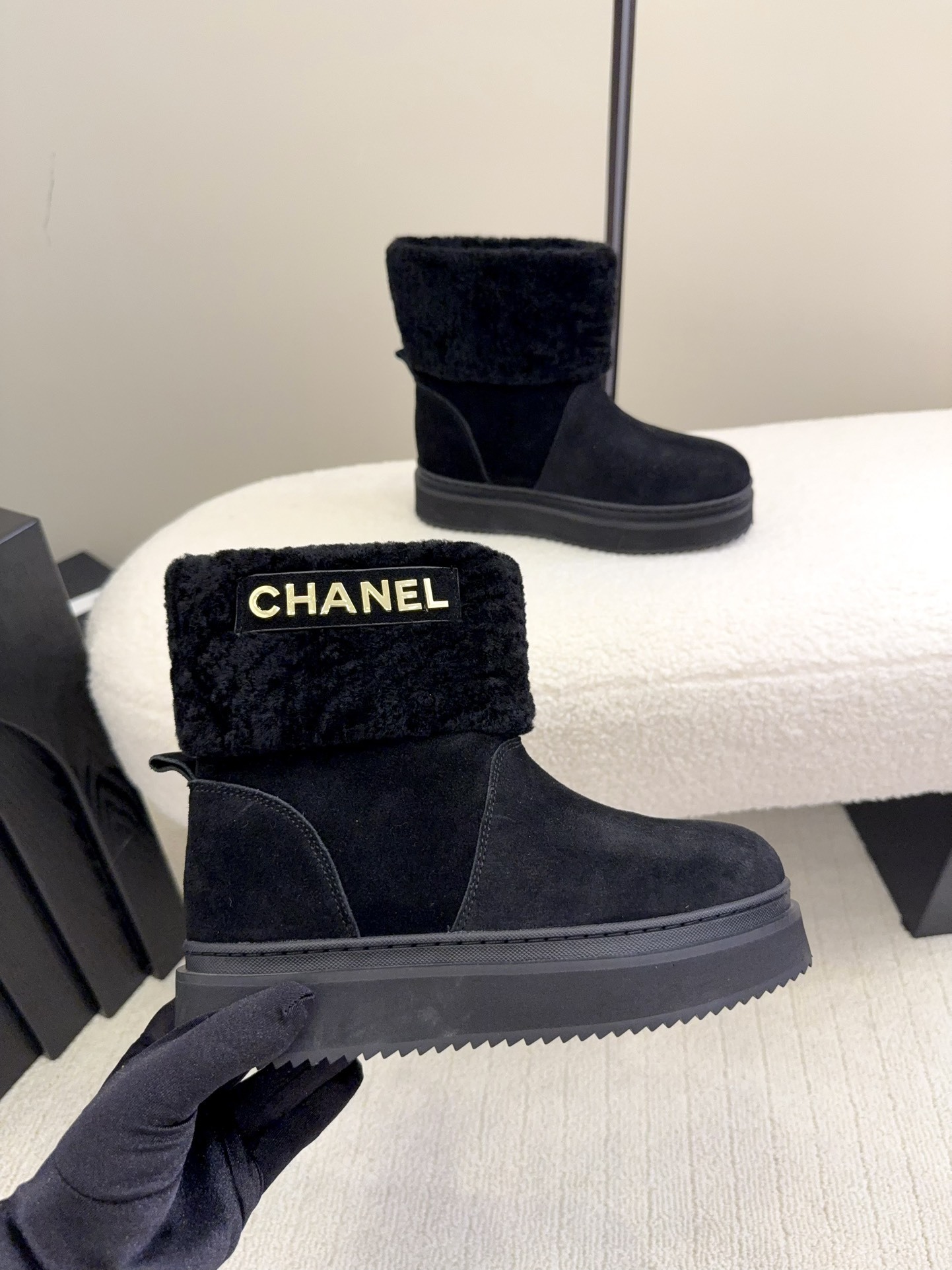Pair of black Chanel suede ankle boots with faux fur trim and gold logo on a white surface - Hình 4