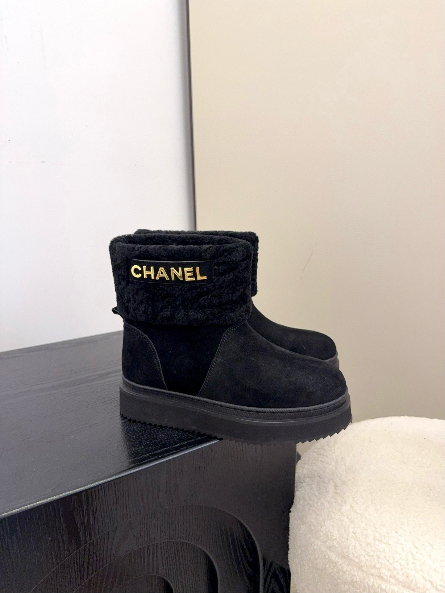 Pair of black Chanel suede ankle boots with faux fur trim and gold logo on a white surface - Hình 3