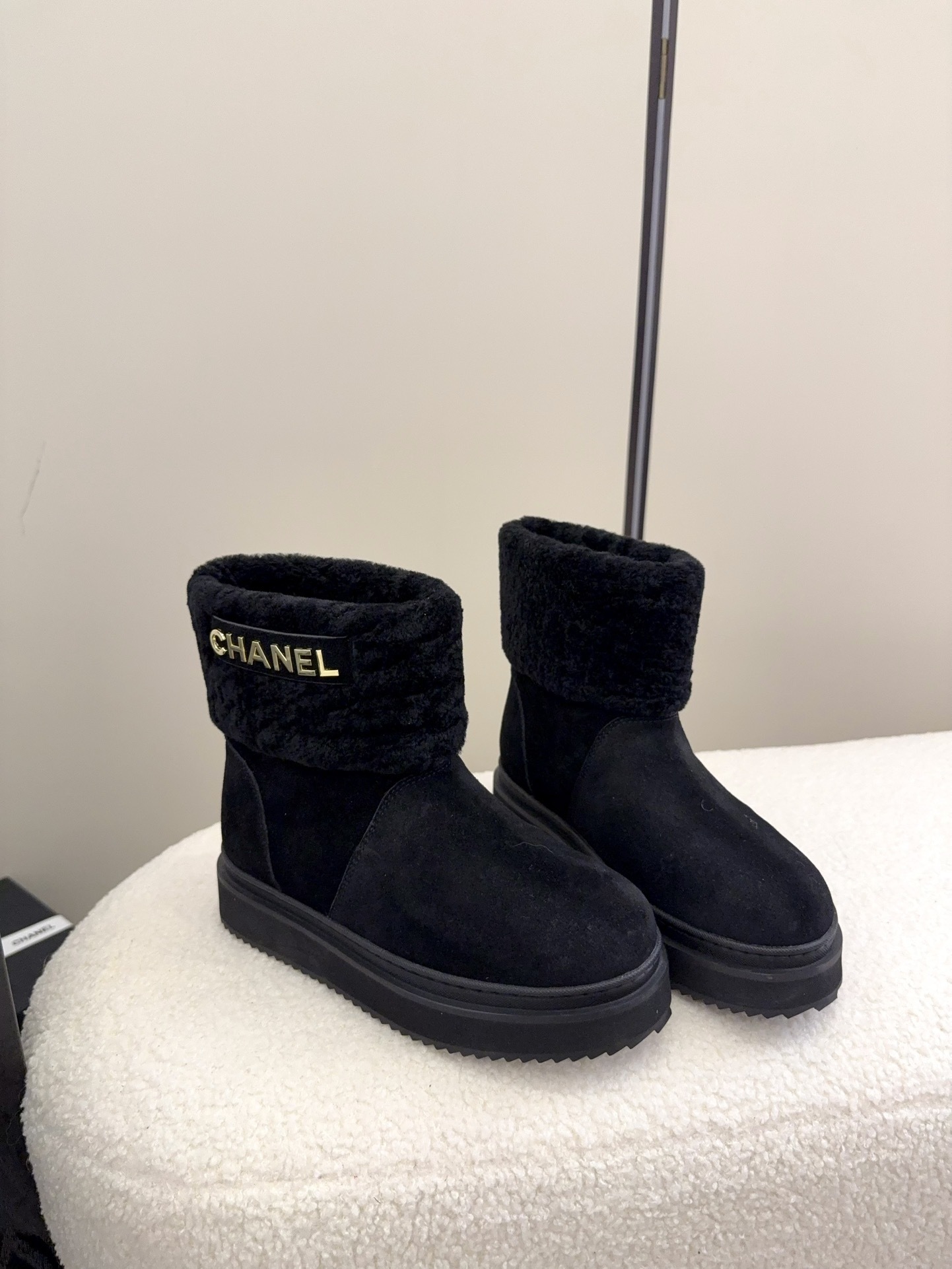 Pair of black Chanel suede ankle boots with faux fur trim and gold logo on a white surface - Hình 2