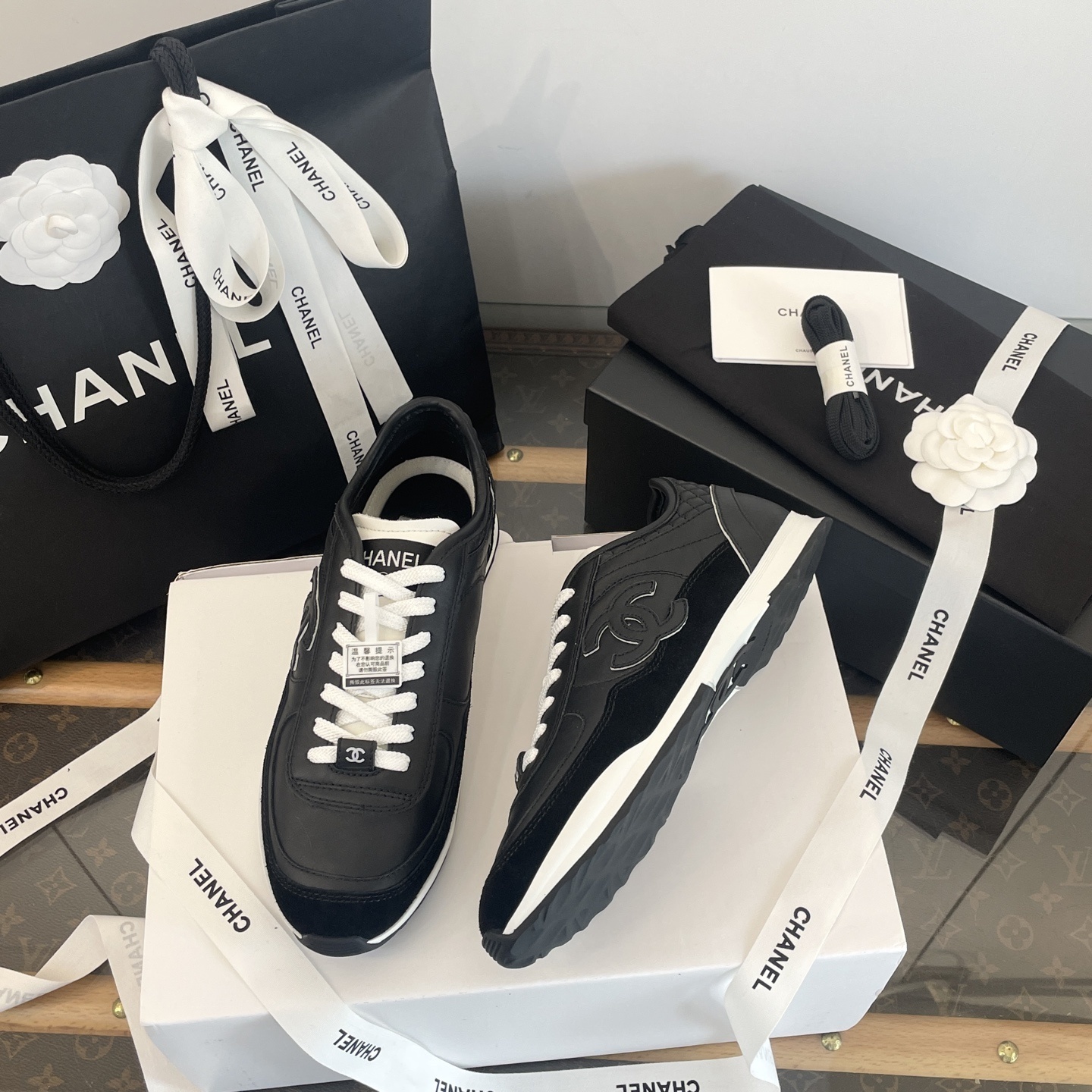 A pair of black Chanel leather sneakers with white laces displayed in original luxury packaging including a box and shopping bag. - Hình 7