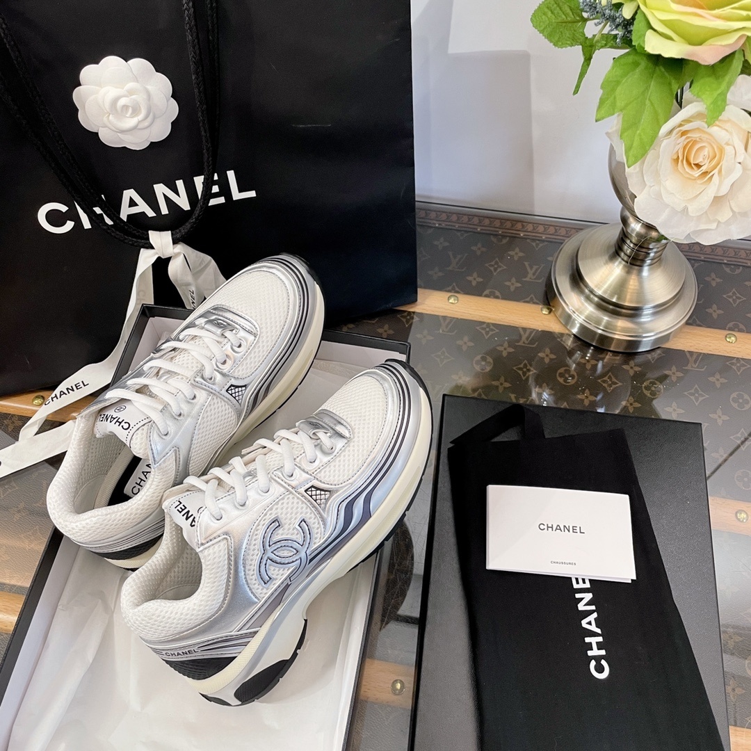 Pair of Chanel metallic silver and white mesh sneakers on a black box with a luxury shopping bag. - Hình 8