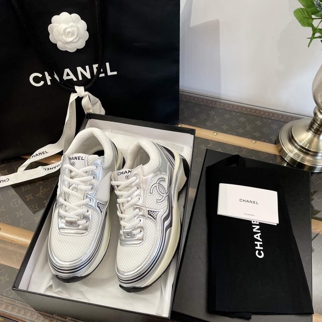 Pair of Chanel metallic silver and white mesh sneakers on a black box with a luxury shopping bag. - Hình 7