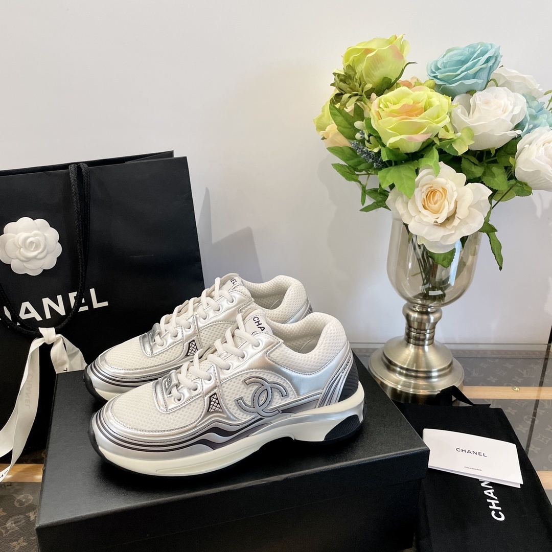 Pair of Chanel metallic silver and white mesh sneakers on a black box with a luxury shopping bag. - Hình 5