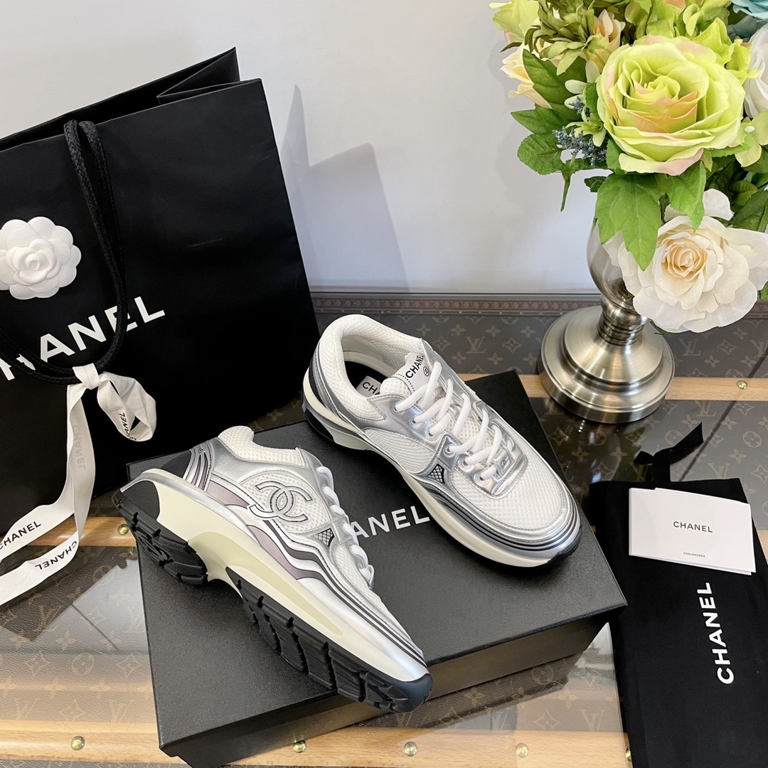 Pair of Chanel metallic silver and white mesh sneakers on a black box with a luxury shopping bag. - Hình 4