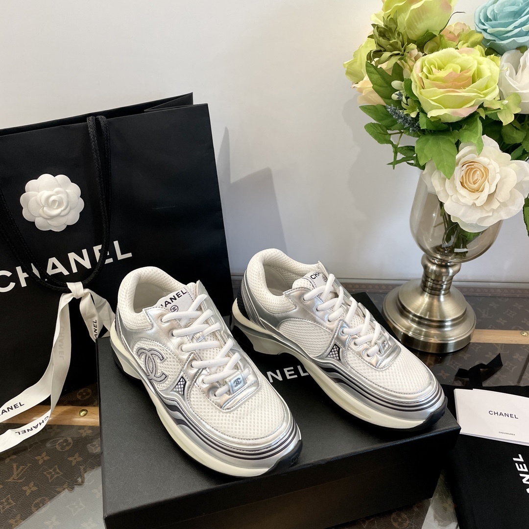 Pair of Chanel metallic silver and white mesh sneakers on a black box with a luxury shopping bag. - Hình 3