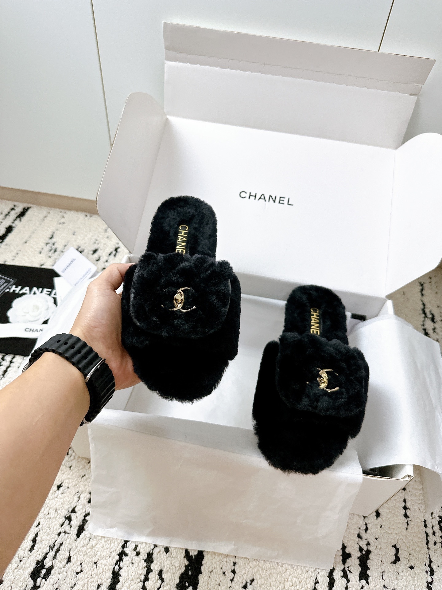 A pair of black plush shearling Chanel slippers featuring gold interlocking CC logos, presented in their original white designer box. - Hình 9