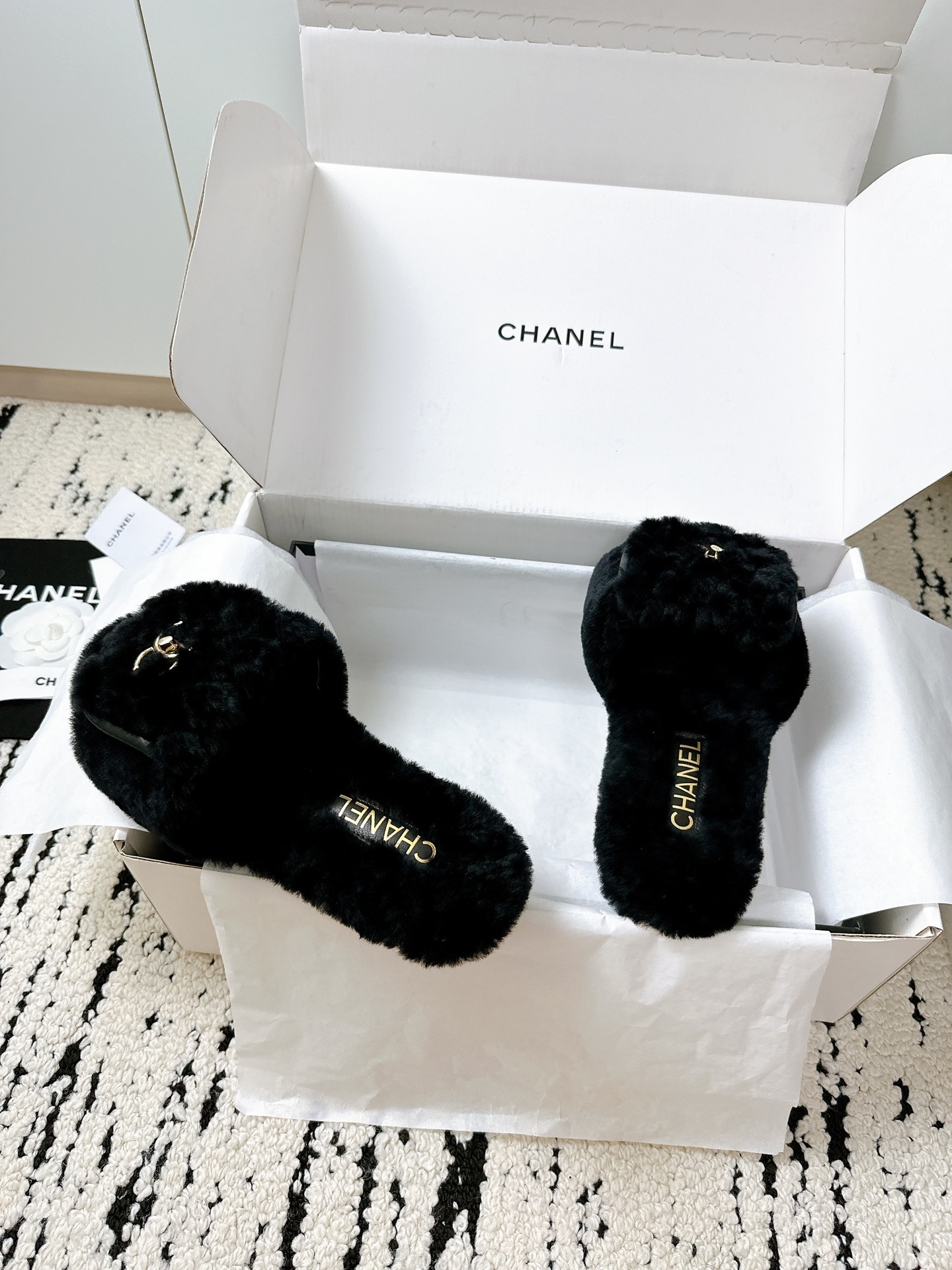 A pair of black plush shearling Chanel slippers featuring gold interlocking CC logos, presented in their original white designer box. - Hình 7