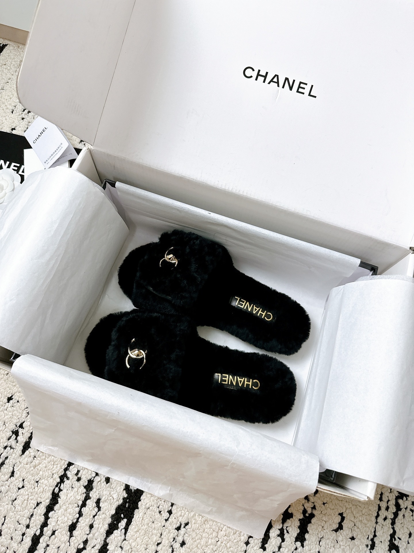 A pair of black plush shearling Chanel slippers featuring gold interlocking CC logos, presented in their original white designer box. - Hình 6