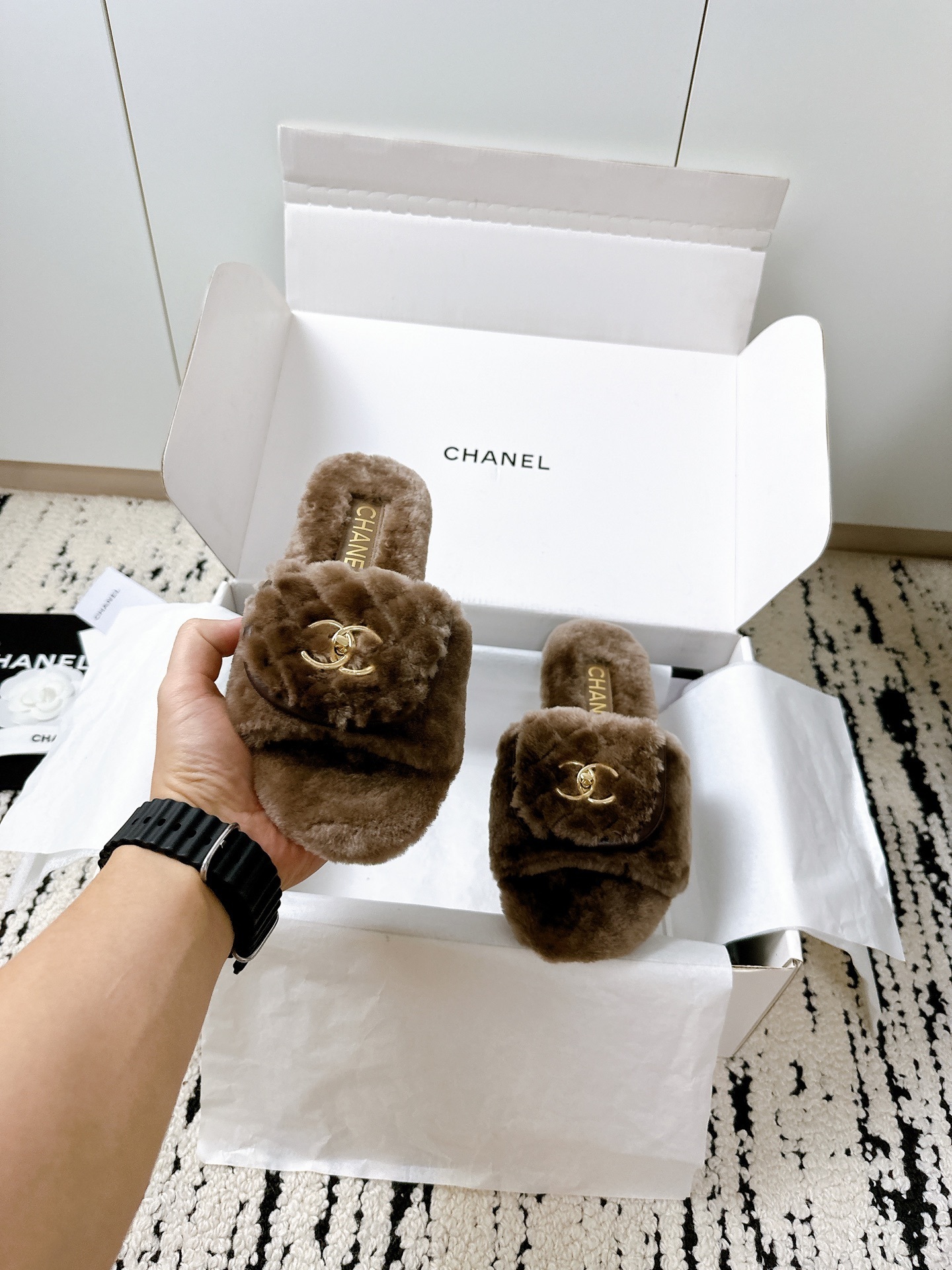 A pair of luxurious brown Chanel quilted shearling fur slippers with gold CC logo displayed in a white designer box. - Hình 7