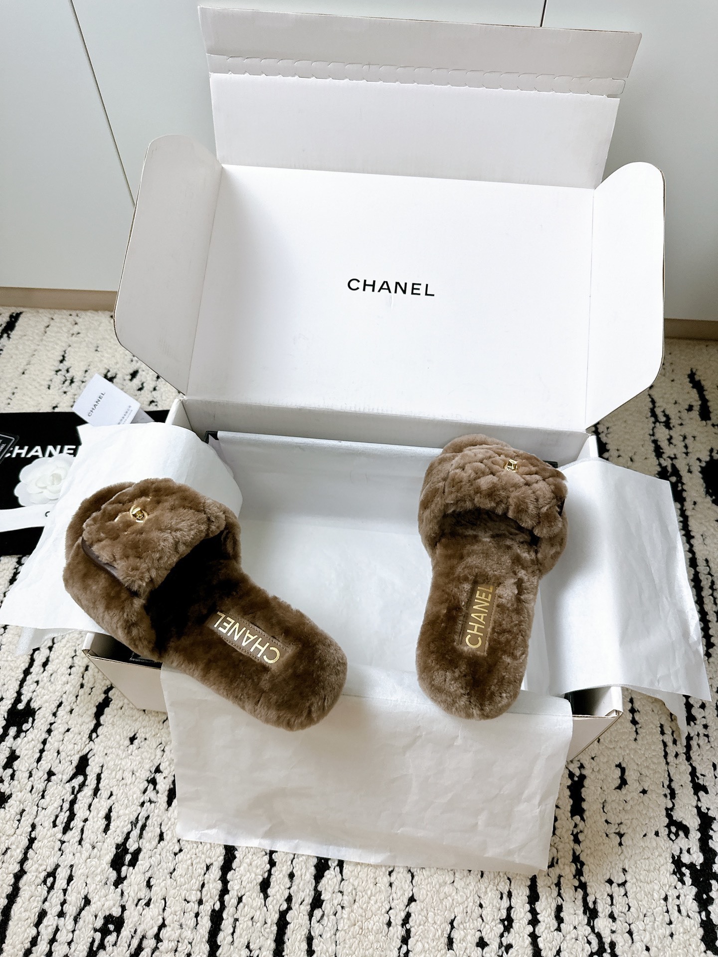 A pair of luxurious brown Chanel quilted shearling fur slippers with gold CC logo displayed in a white designer box. - Hình 6