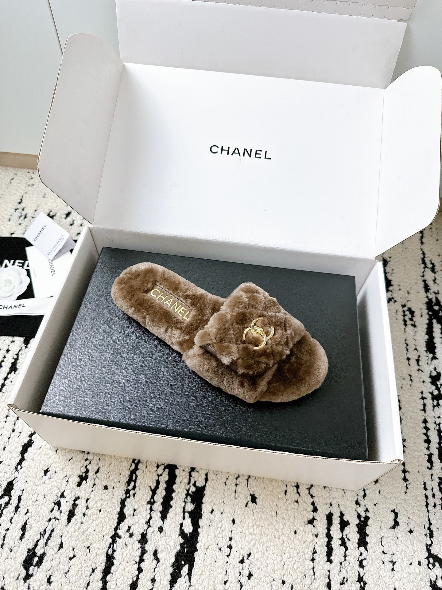 A pair of luxurious brown Chanel quilted shearling fur slippers with gold CC logo displayed in a white designer box. - Hình 2