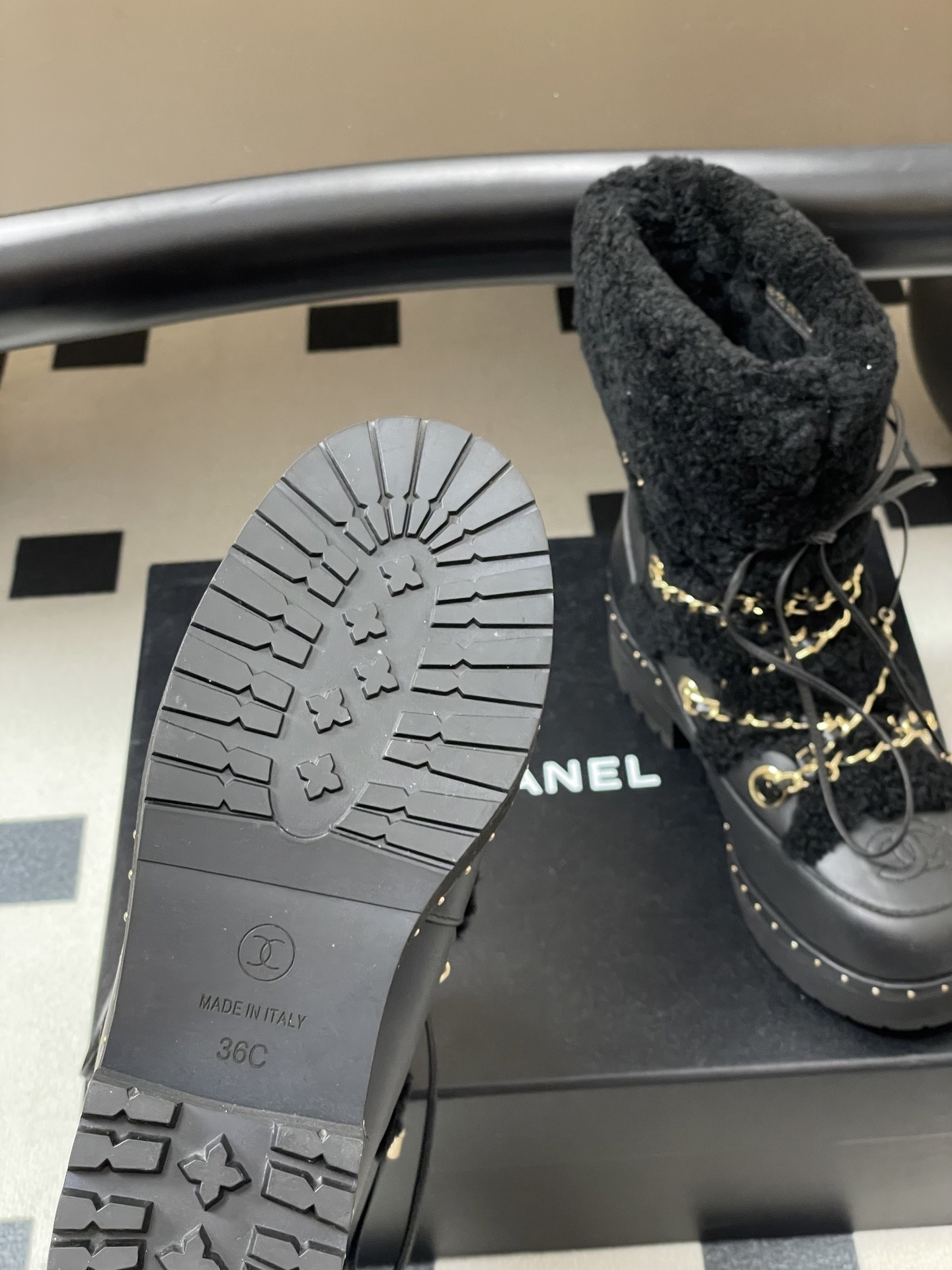 Pair of black leather combat boots with black shearling trim, gold chain detailing, and lace-up front on a black pedestal. - Hình 10