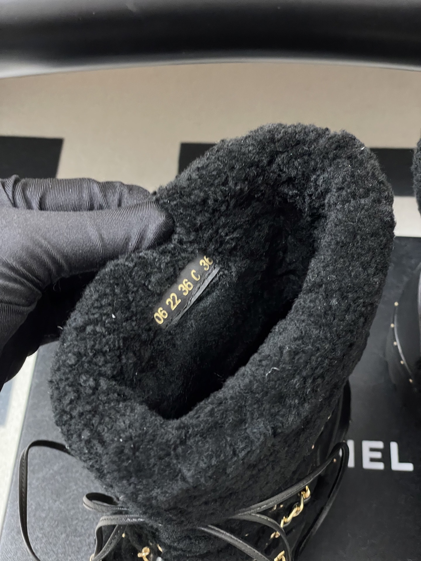 Pair of black leather combat boots with black shearling trim, gold chain detailing, and lace-up front on a black pedestal. - Hình 9