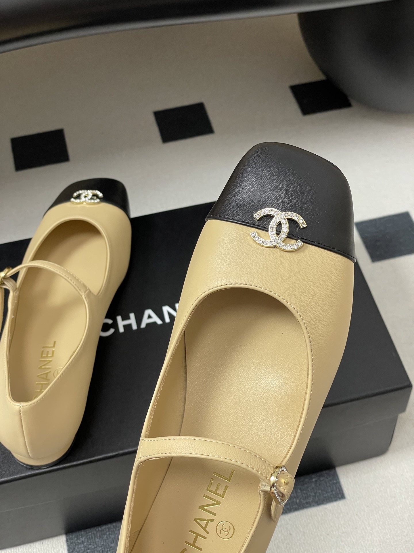 Pair of beige and black Chanel Mary Jane flats with crystal CC logos and rhinestone buckles on a black table - Hình 9