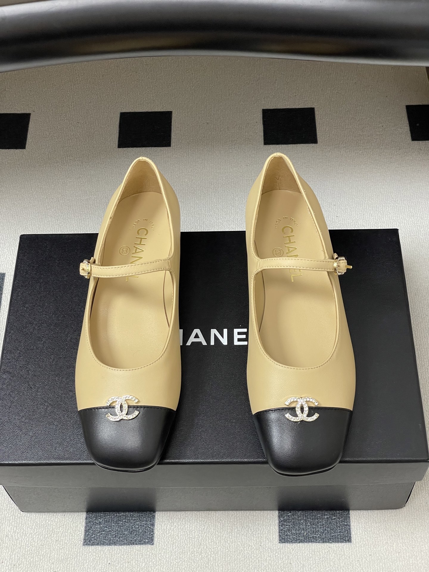 Pair of beige and black Chanel Mary Jane flats with crystal CC logos and rhinestone buckles on a black table - Hình 5