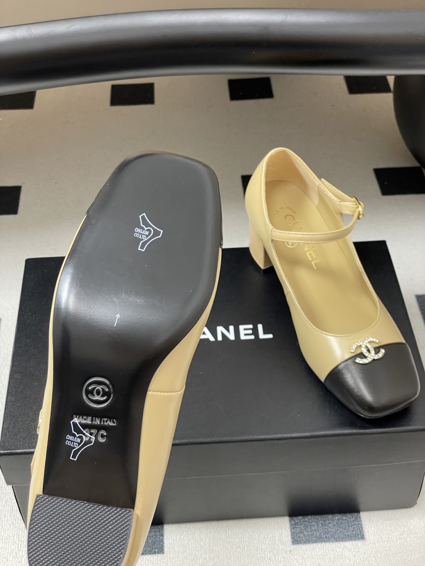 A pair of beige and black two-tone Mary Jane block heel shoes with crystal CC logos on a black table. - Hình 8