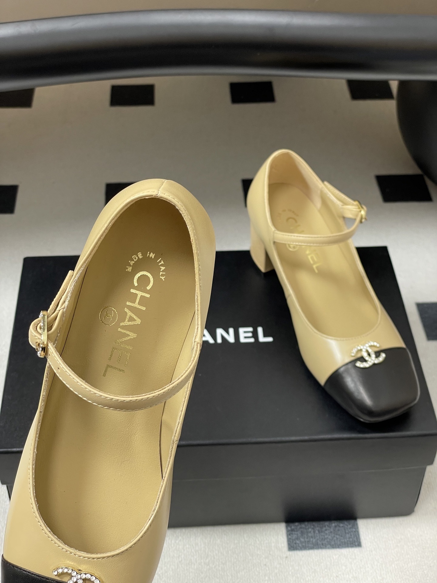A pair of beige and black two-tone Mary Jane block heel shoes with crystal CC logos on a black table. - Hình 7