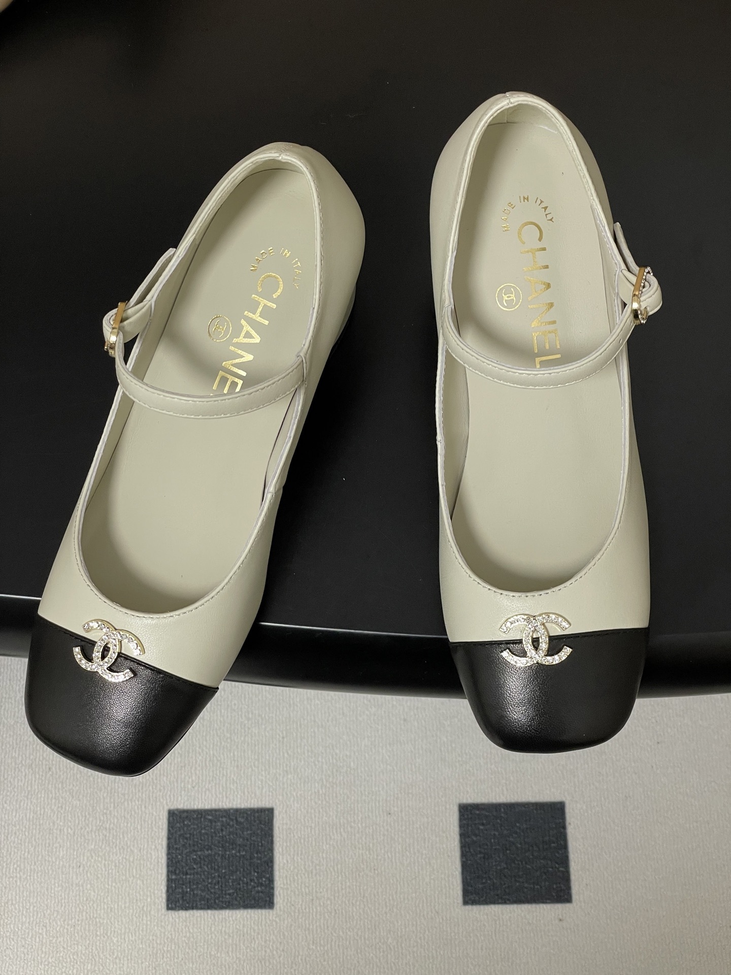 A pair of cream and black two-tone Mary Jane block heels featuring a crystal-embellished logo on the toe cap. - Hình 2