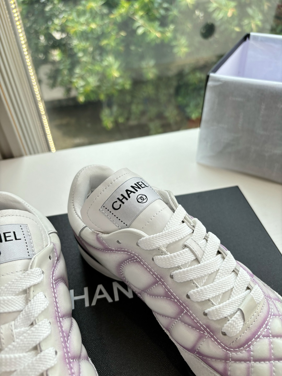 A pair of Chanel white and purple quilted leather sneakers with CC logo displayed in a box - Hình 8