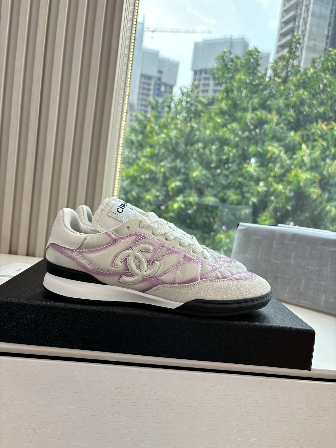 A pair of Chanel white and purple quilted leather sneakers with CC logo displayed in a box - Hình 7