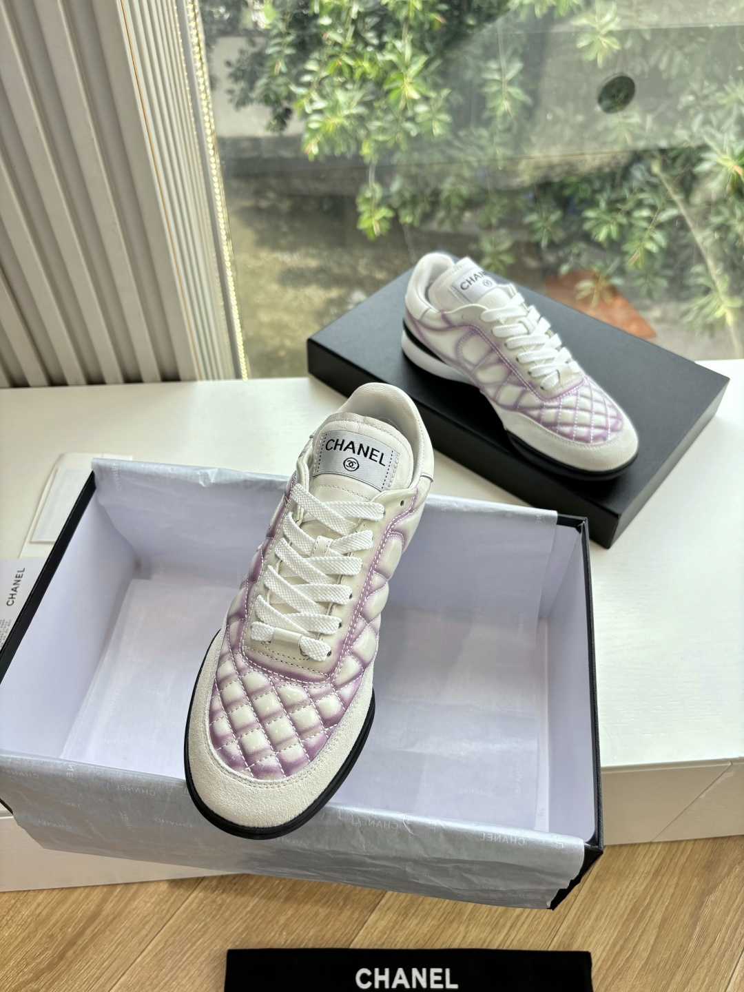 A pair of Chanel white and purple quilted leather sneakers with CC logo displayed in a box - Hình 5