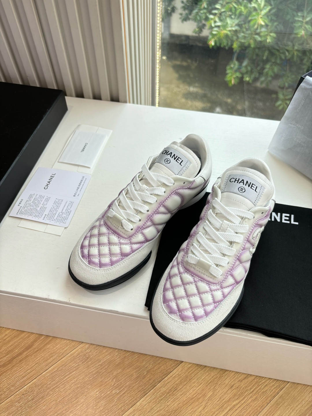 A pair of Chanel white and purple quilted leather sneakers with CC logo displayed in a box - Hình 3
