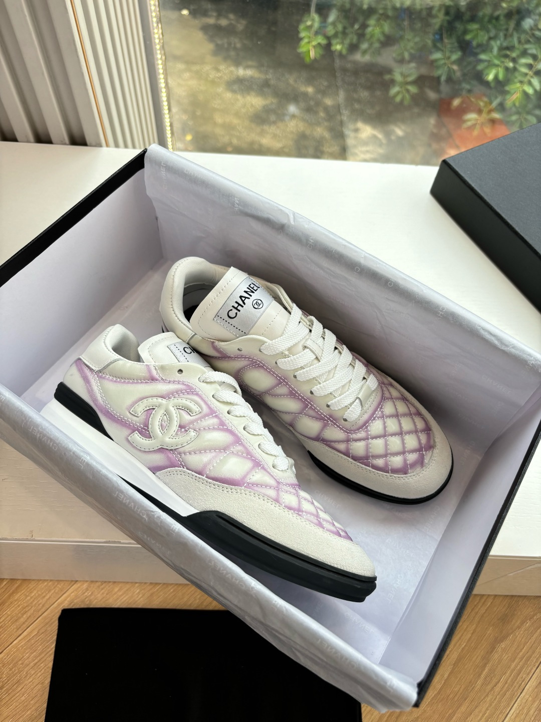 A pair of Chanel white and purple quilted leather sneakers with CC logo displayed in a box - Hình 2