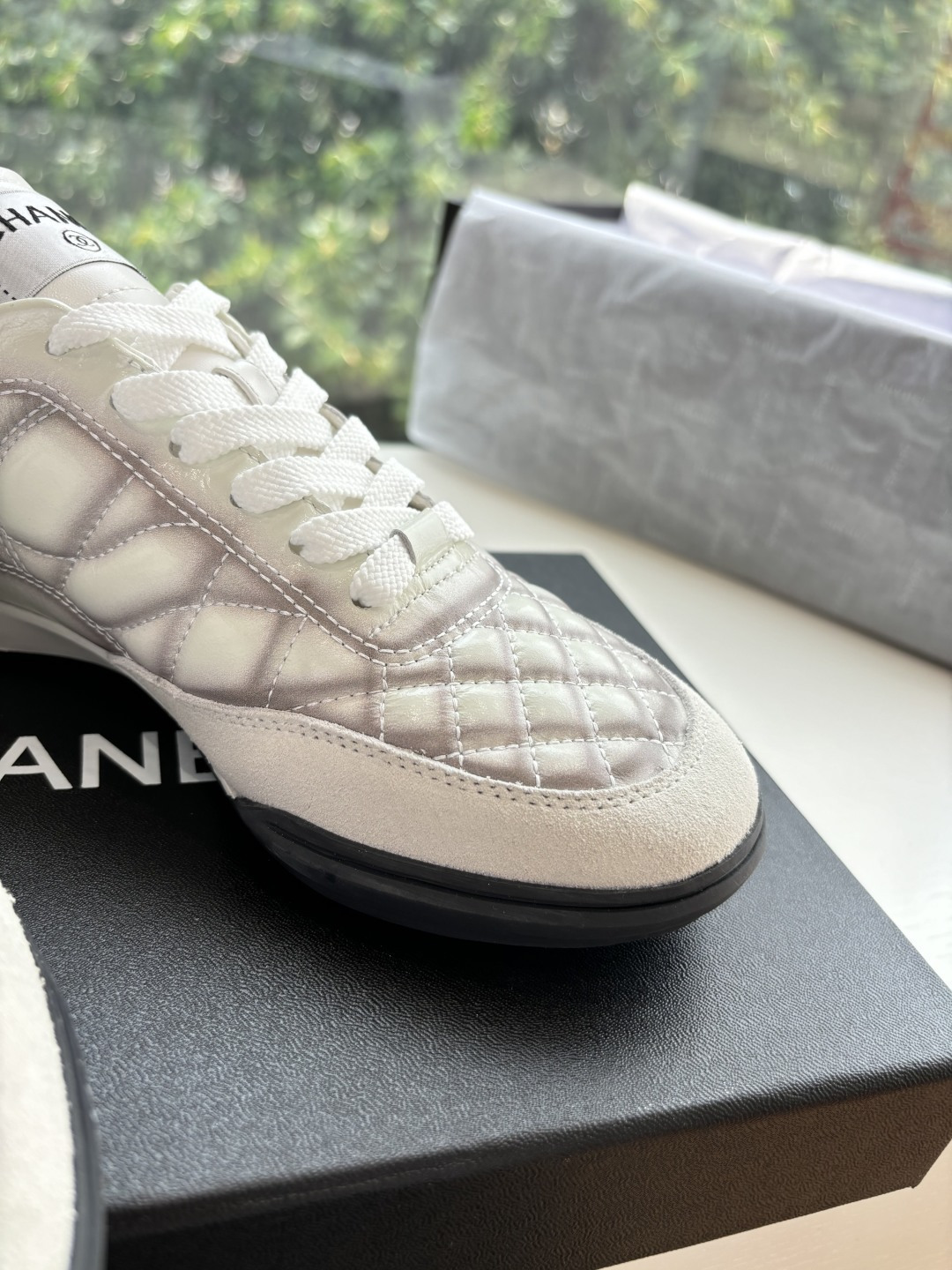 A pair of premium Chanel white quilted sneakers with grey shadow detailing and interlocking CC logo, displayed in their original black box. - Hình 9