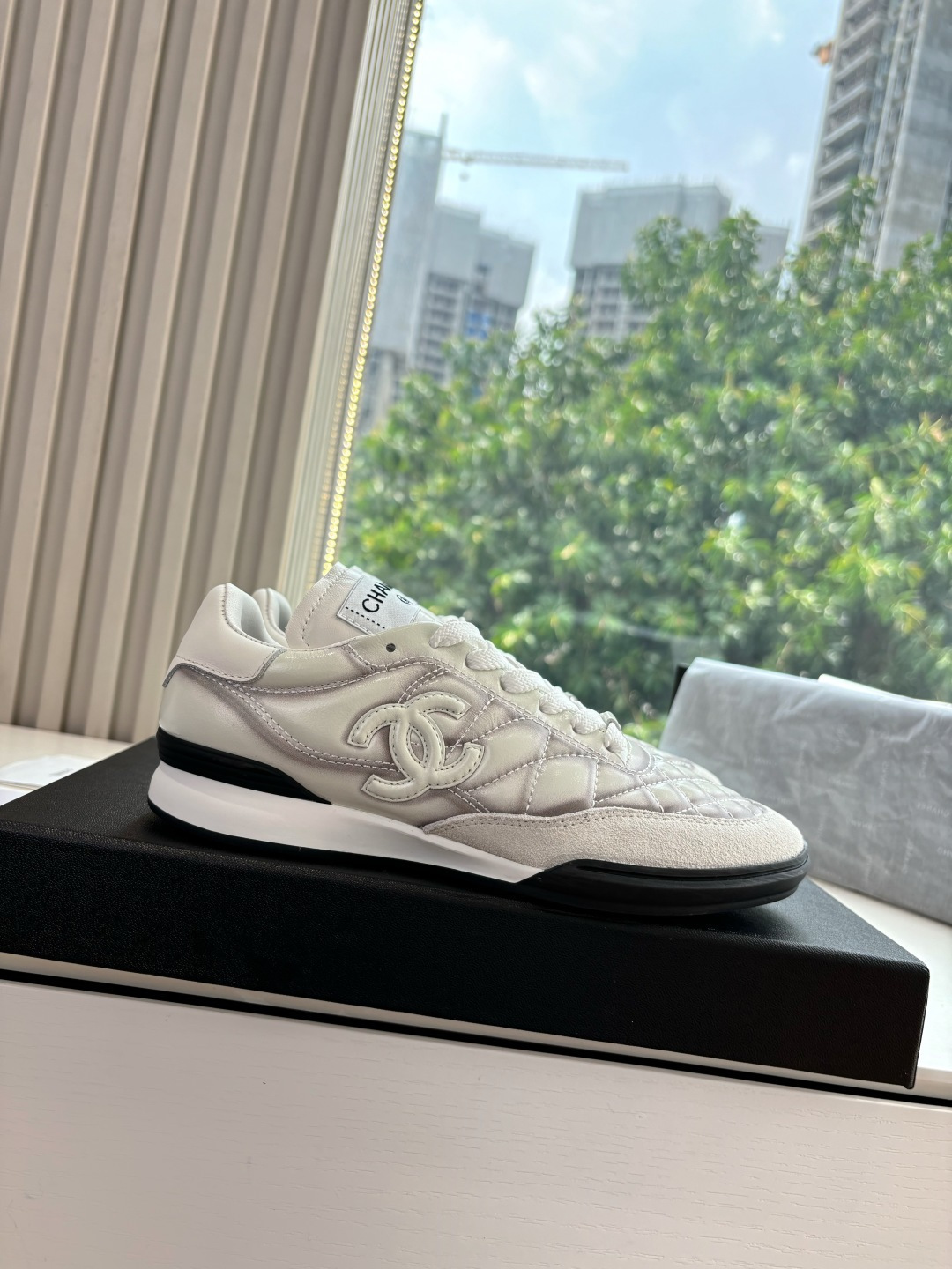 A pair of premium Chanel white quilted sneakers with grey shadow detailing and interlocking CC logo, displayed in their original black box. - Hình 7