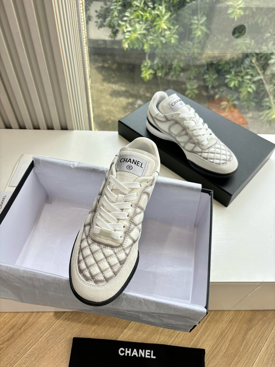 A pair of premium Chanel white quilted sneakers with grey shadow detailing and interlocking CC logo, displayed in their original black box. - Hình 4