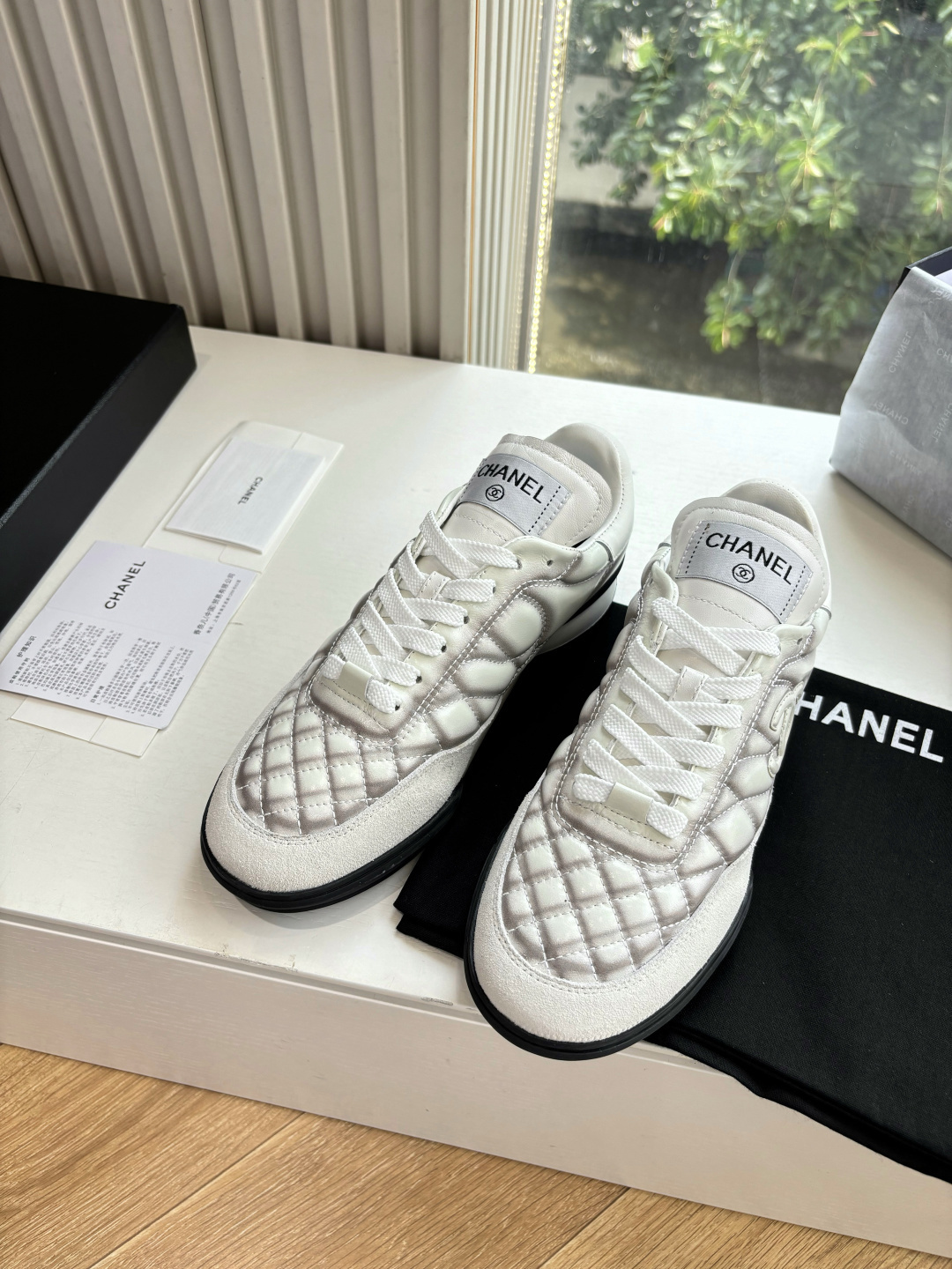 A pair of premium Chanel white quilted sneakers with grey shadow detailing and interlocking CC logo, displayed in their original black box. - Hình 3