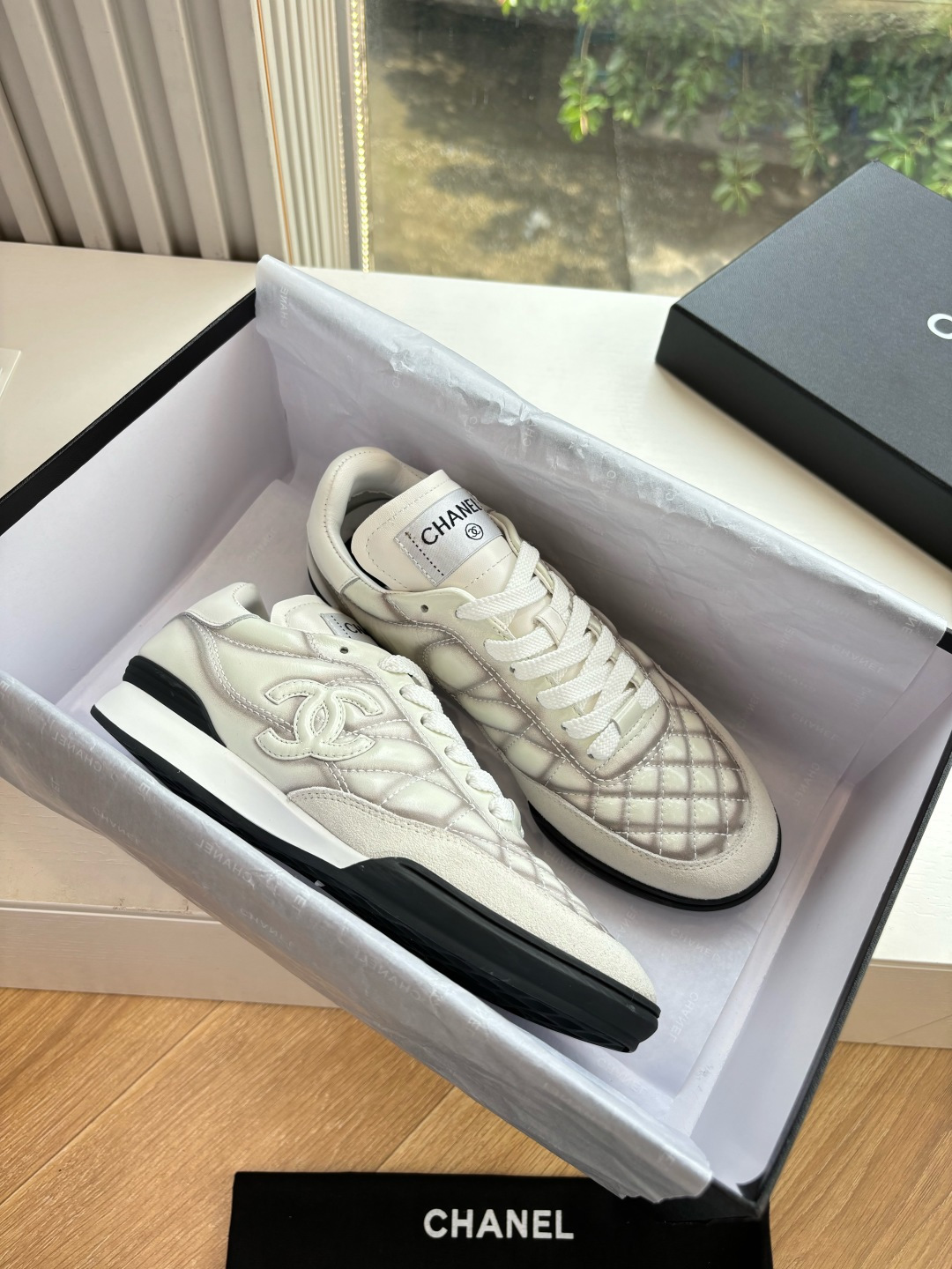 A pair of premium Chanel white quilted sneakers with grey shadow detailing and interlocking CC logo, displayed in their original black box. - Hình 2