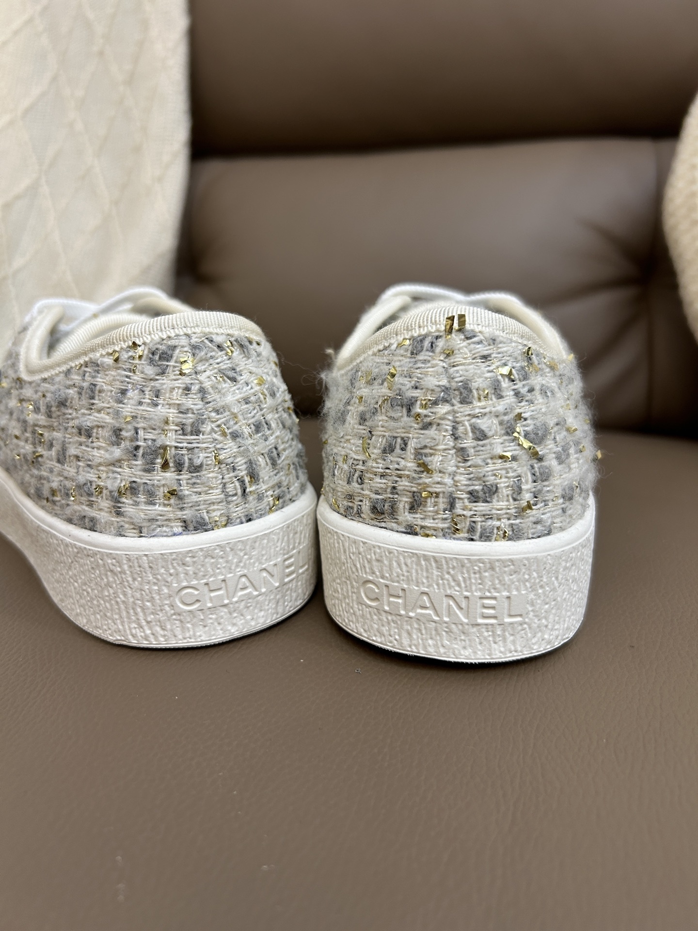 A pair of Chanel luxury low-top sneakers featuring ivory tweed fabric with gold metallic threads and white rubber soles. - Hình 9