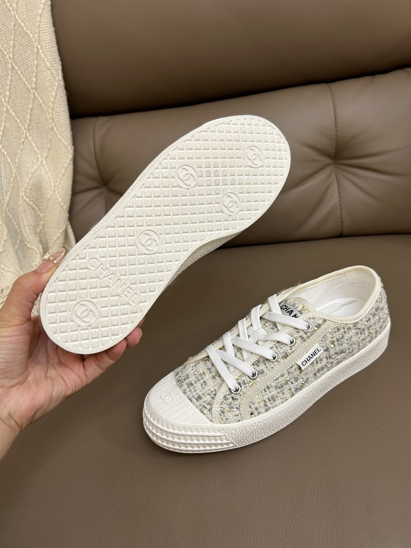 A pair of Chanel luxury low-top sneakers featuring ivory tweed fabric with gold metallic threads and white rubber soles. - Hình 7