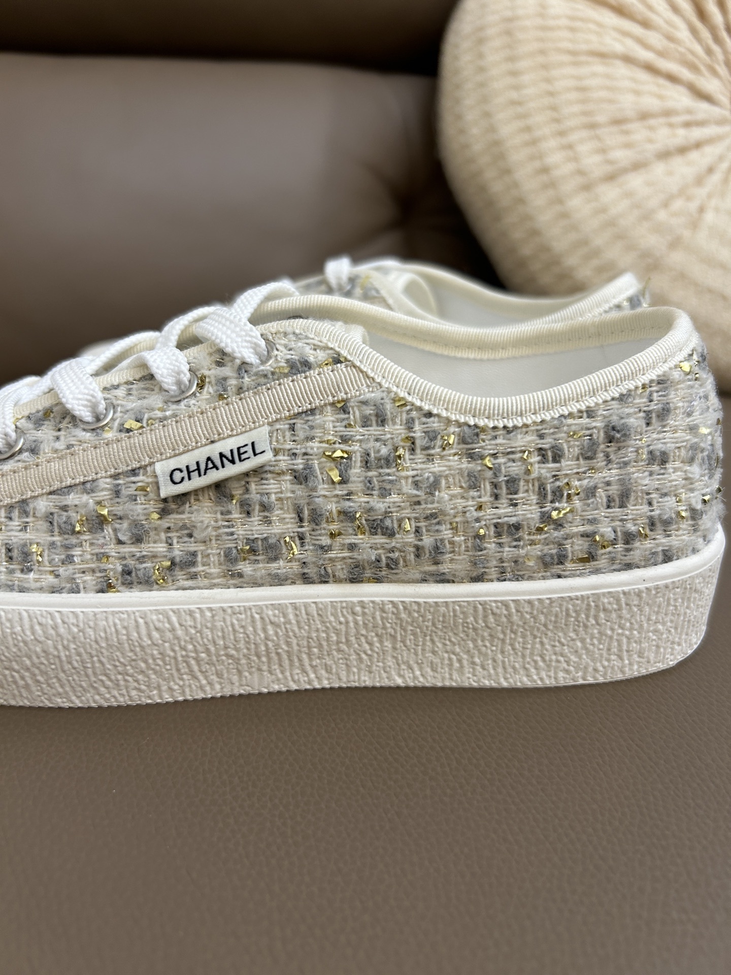 A pair of Chanel luxury low-top sneakers featuring ivory tweed fabric with gold metallic threads and white rubber soles. - Hình 6