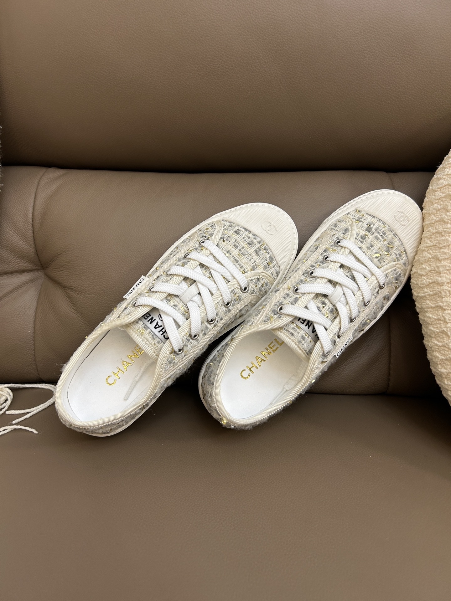 A pair of Chanel luxury low-top sneakers featuring ivory tweed fabric with gold metallic threads and white rubber soles. - Hình 5