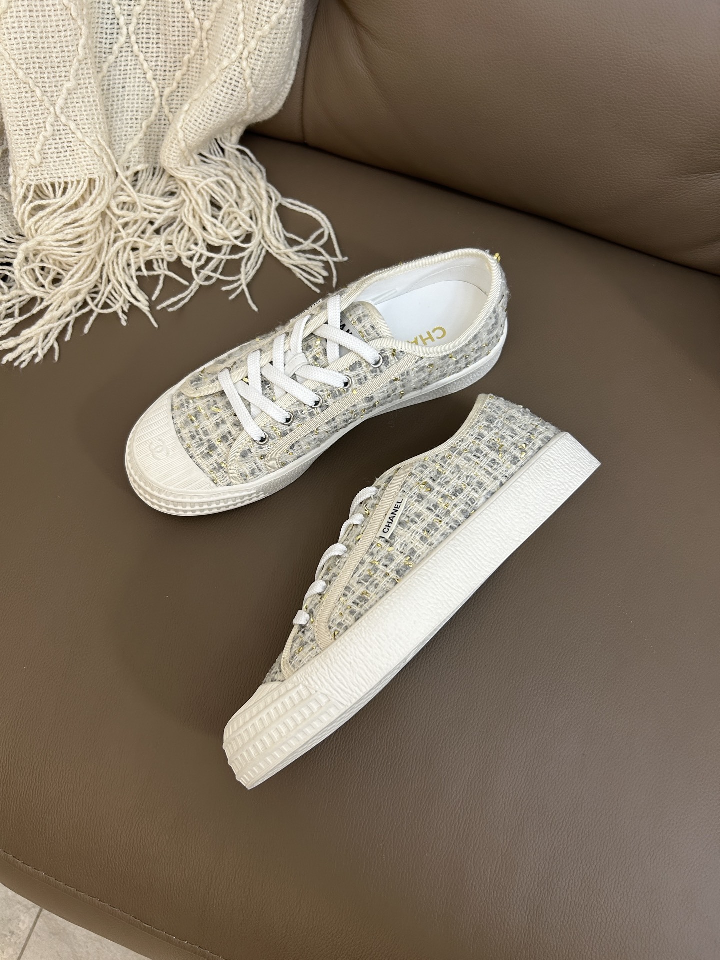 A pair of Chanel luxury low-top sneakers featuring ivory tweed fabric with gold metallic threads and white rubber soles. - Hình 4