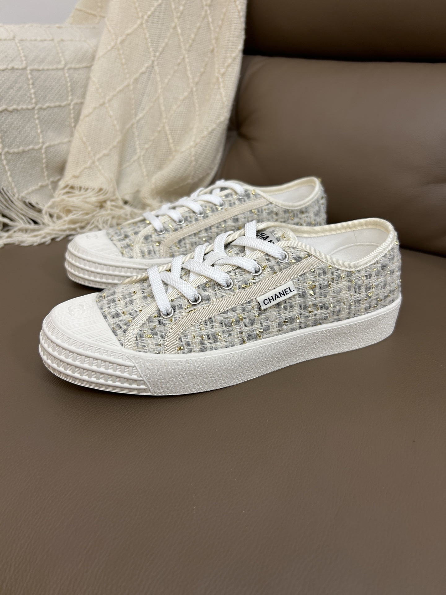 A pair of Chanel luxury low-top sneakers featuring ivory tweed fabric with gold metallic threads and white rubber soles. - Hình 3