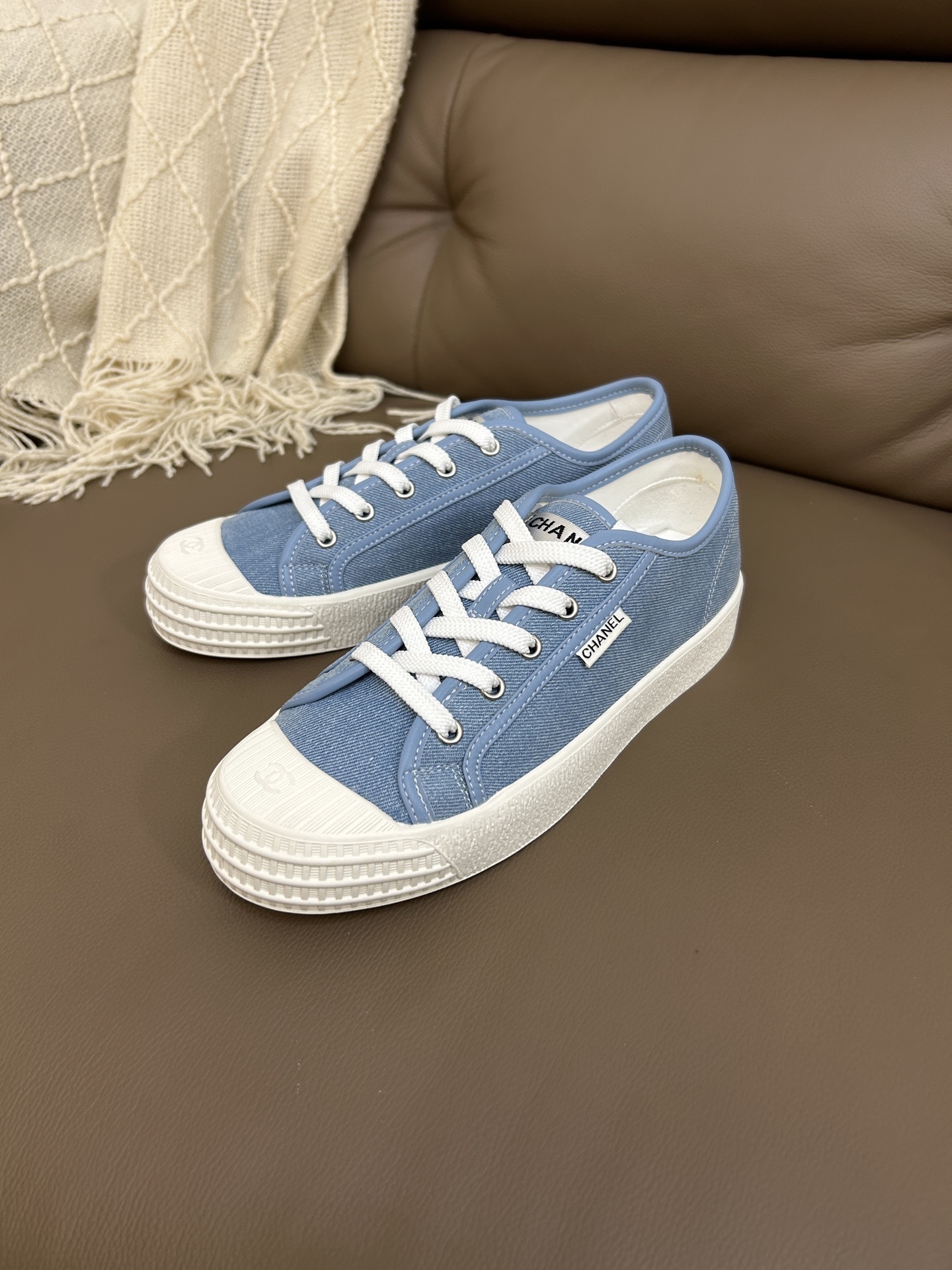 A pair of Chanel light blue denim low-top sneakers with white laces and embossed CC logo on the toe cap. - Hình 8
